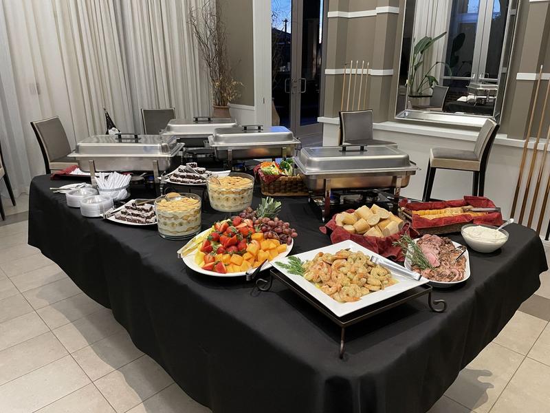 Catered buffet on black linens with chafing dishes, a fresh fruit platter, shrimp, sliced roast and a basket of rolls