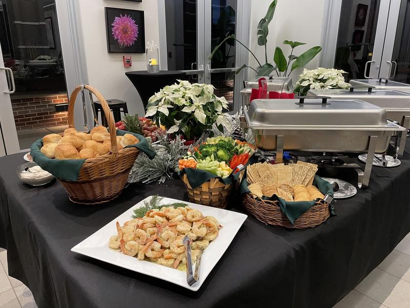 Holiday buffet with a shrimp platter, baskets of rolls and crackers, fresh vegetables and white poinsettias on black linens