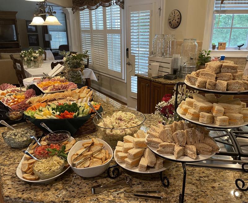 Home party spread with tiered stands of tea sandwiches, salads, dips and appetizer platters on a kitchen counter