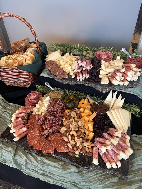 Two stone serving boards of cured meats, cheeses, nuts and dried fruit with a basket of crackers