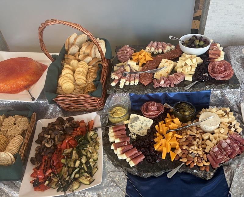 Tiered charcuterie boards with a grilled vegetable platter, a cheese ball and bread baskets on a sequined tablecloth