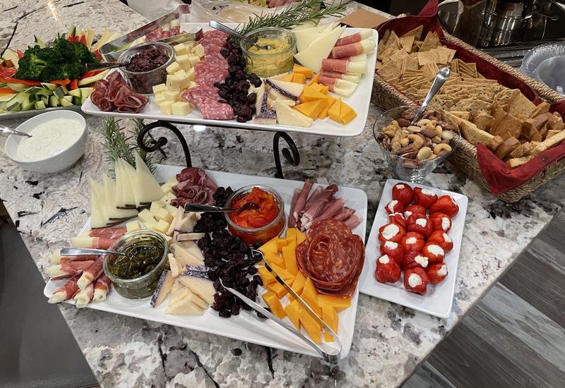 Tiered charcuterie display with cured meats, cheeses, stuffed mini peppers and a basket of crackers