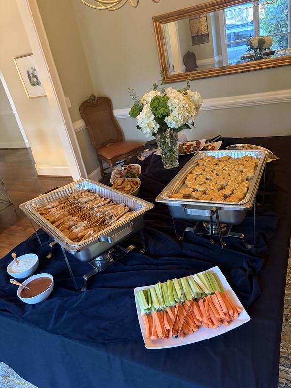Buffalo chicken skewers in buffet chafing dishes beside a platter of celery and carrots