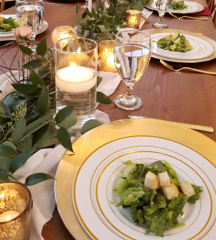 Catered dinner party table set with plated salads and candles
