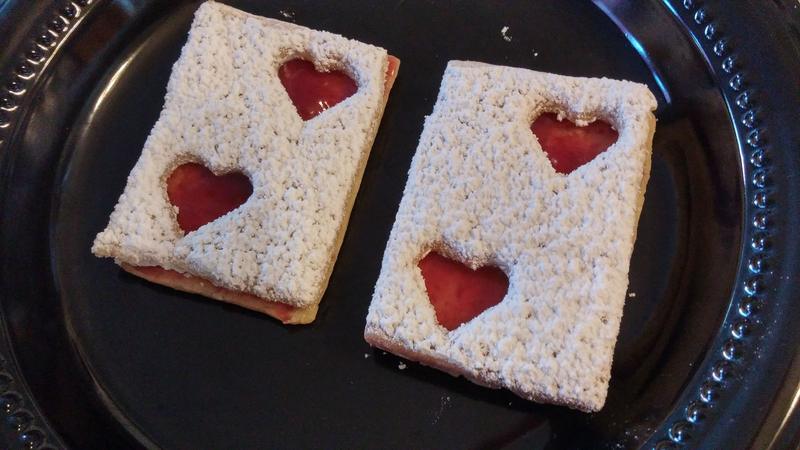 Two square treats with red heart cut-outs on a black plate