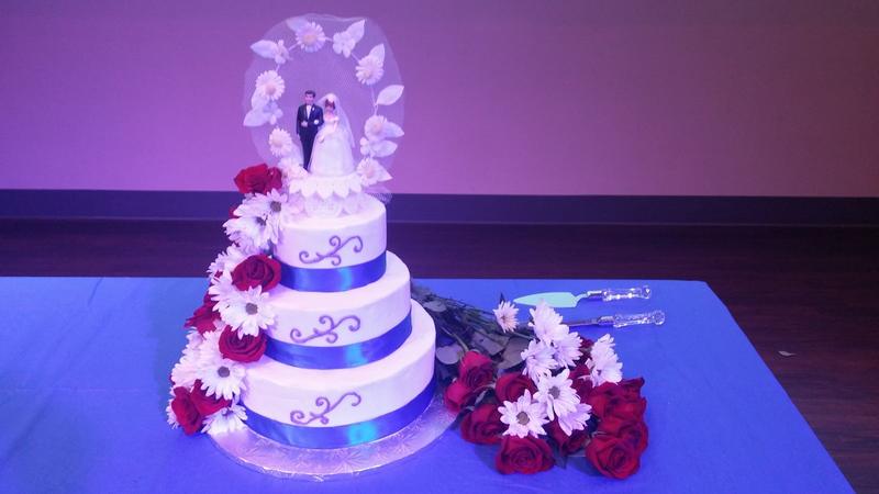 Tiered wedding cake with flowers, displayed under soft purple lighting