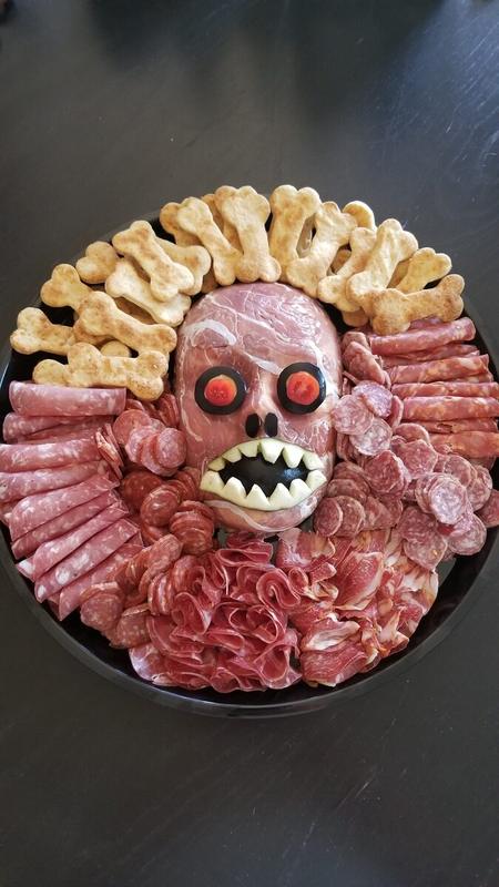 Halloween charcuterie board of cured meats and cheeses arranged around a zombie head