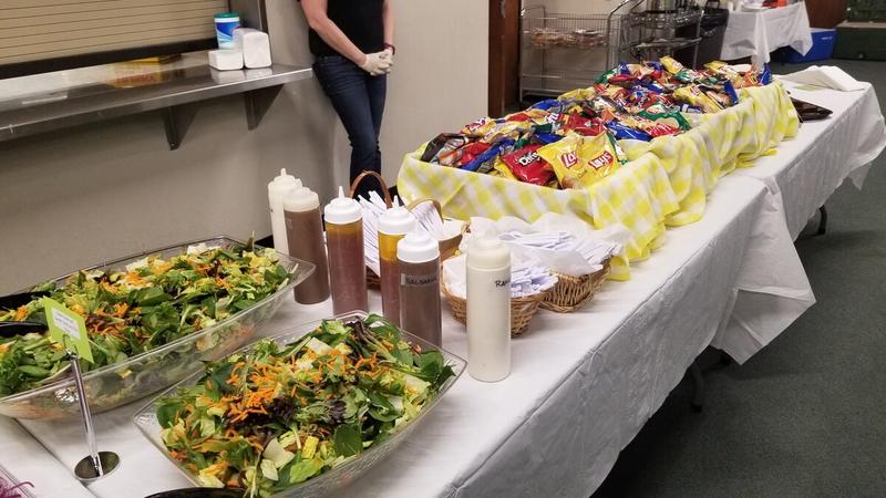 Office catering spread with large salads and individual bags of chips