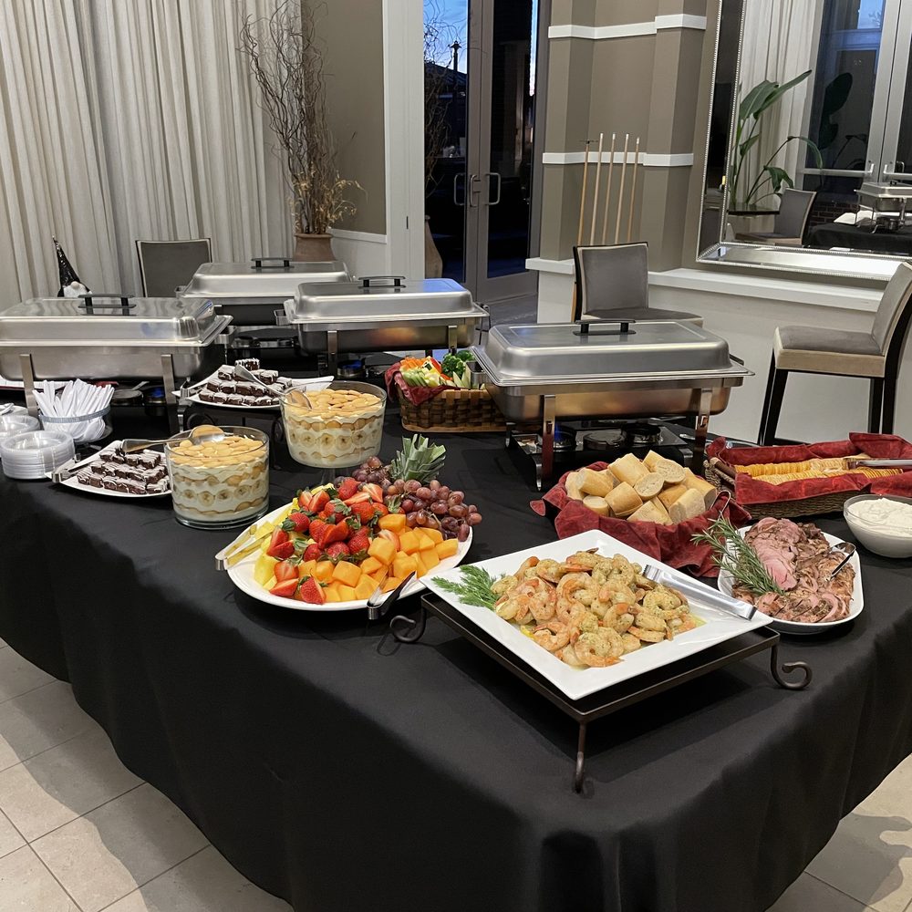 Catered buffet with chafing dishes, a fresh fruit platter and a shrimp platter on black linens